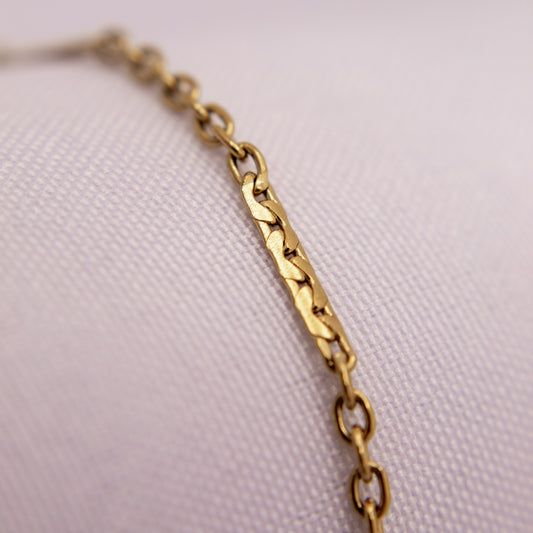 Gold chain bracelet anklet on a light pink textured background