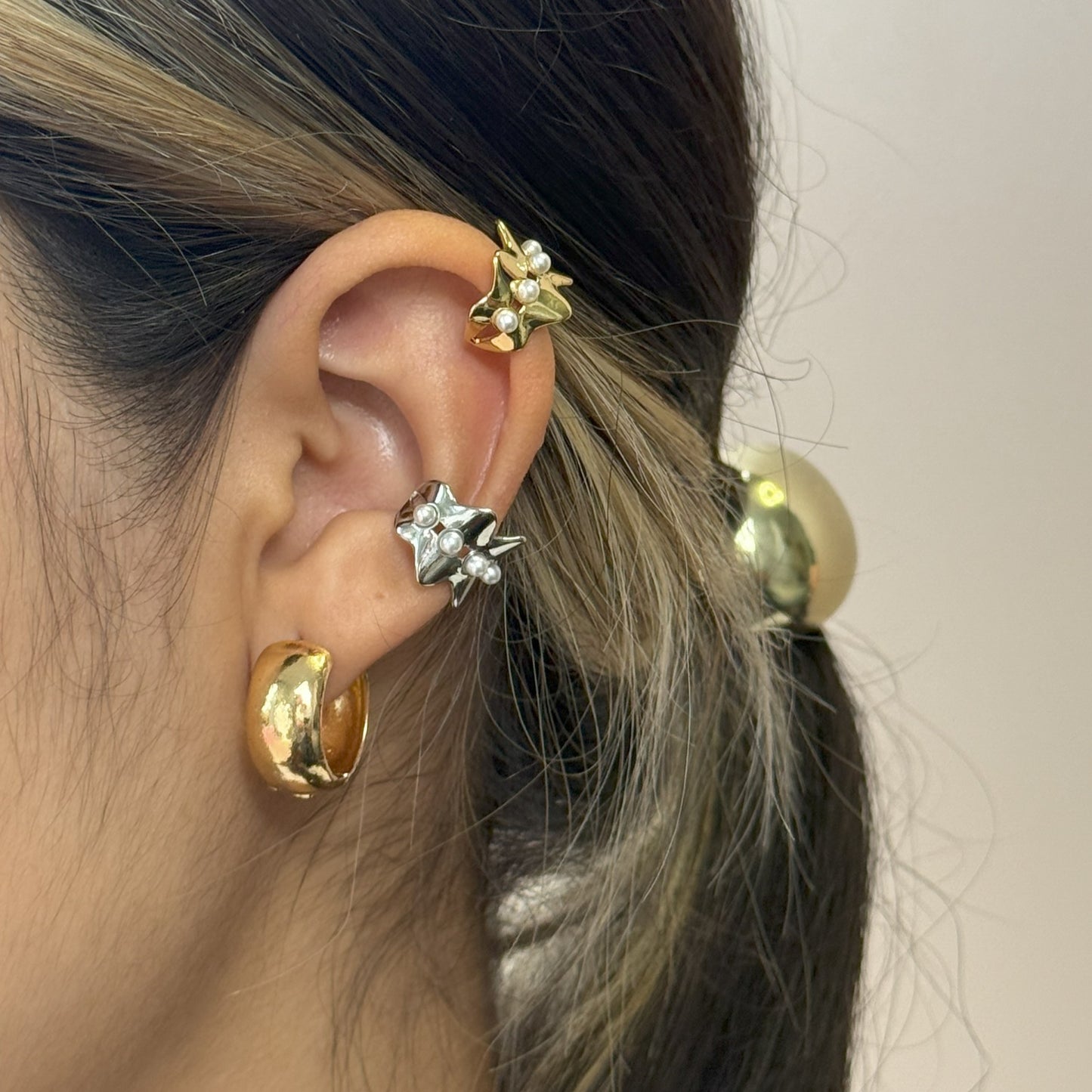 Close-up of an ear with gold and silver earrings against a neutral background