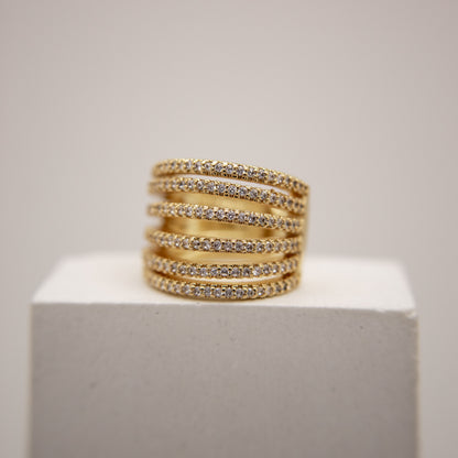Stack of gold ear cuff with embedded stones on a white pedestal against a light gray background