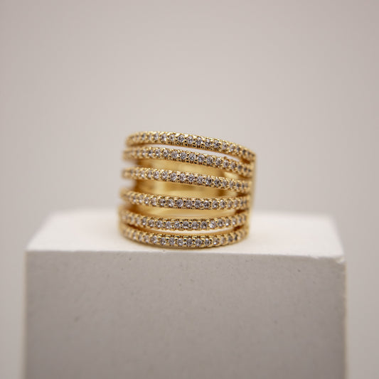Stack of gold ear cuff with embedded stones on a white pedestal against a light gray background