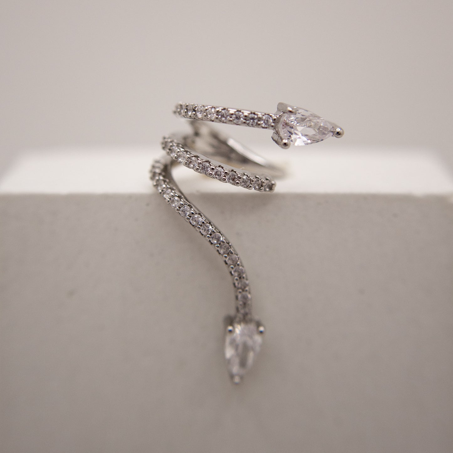 Silver snake-shaped ear cuff with clear gemstones on a light gray background