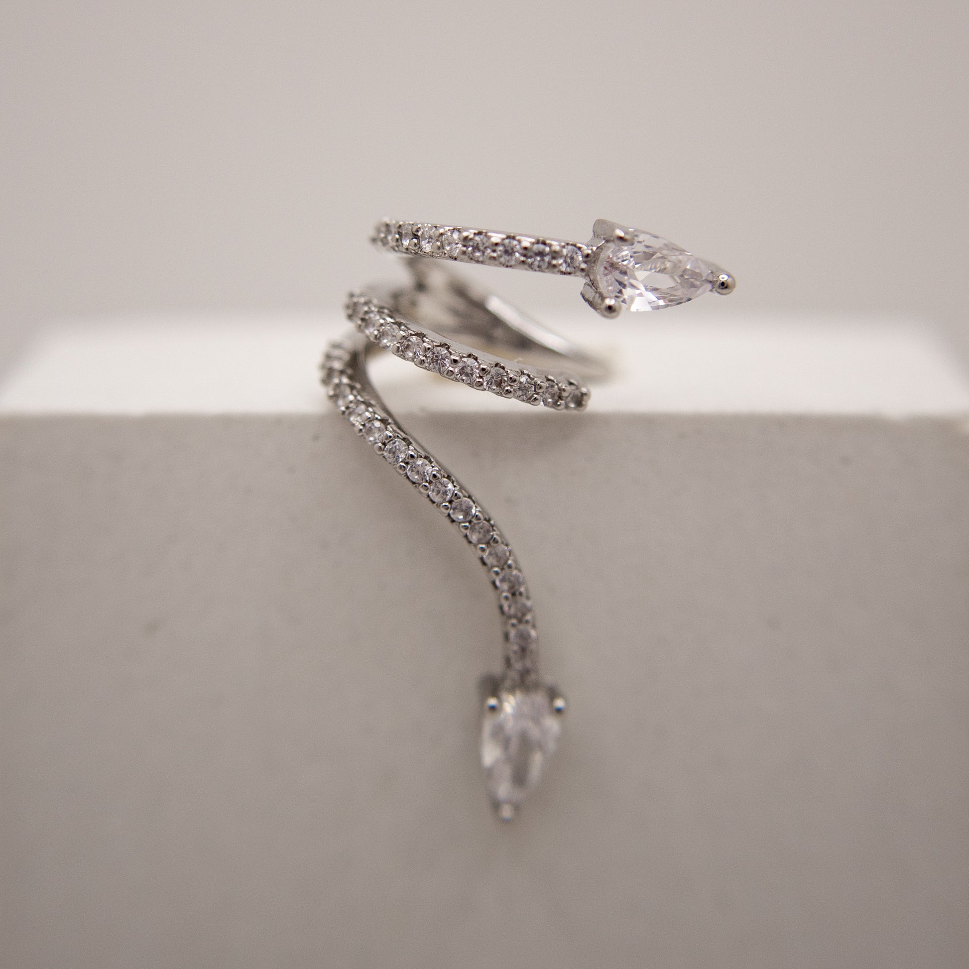 Silver snake-shaped ear cuff with clear gemstones on a light gray background