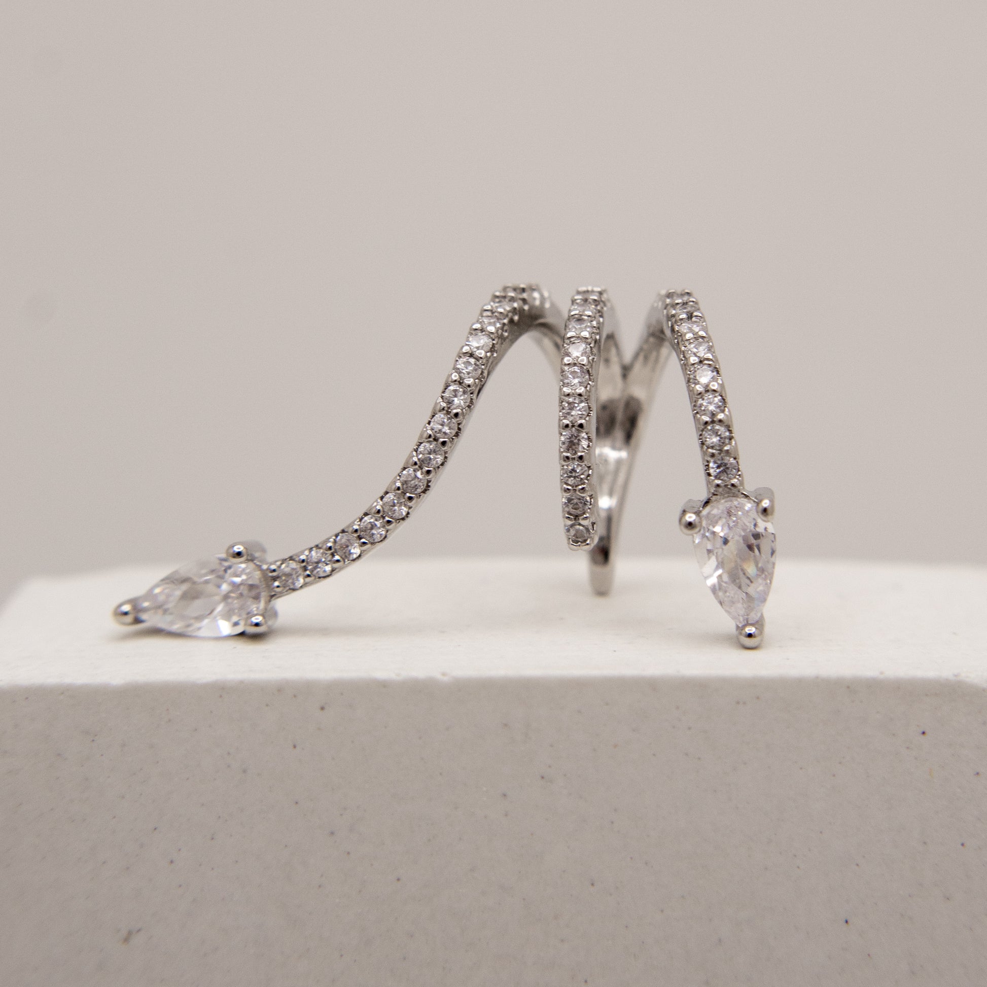 Pair of silver hoop ear cuff with clear gemstones on a light gray background