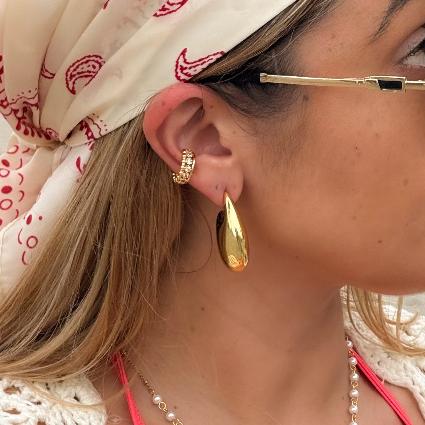 Close-up of a person wearing gold hoop earrings with a patterned headscarf and necklace.