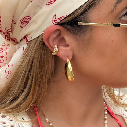 Close-up of a person wearing gold hoop earrings with a patterned headscarf and necklace.