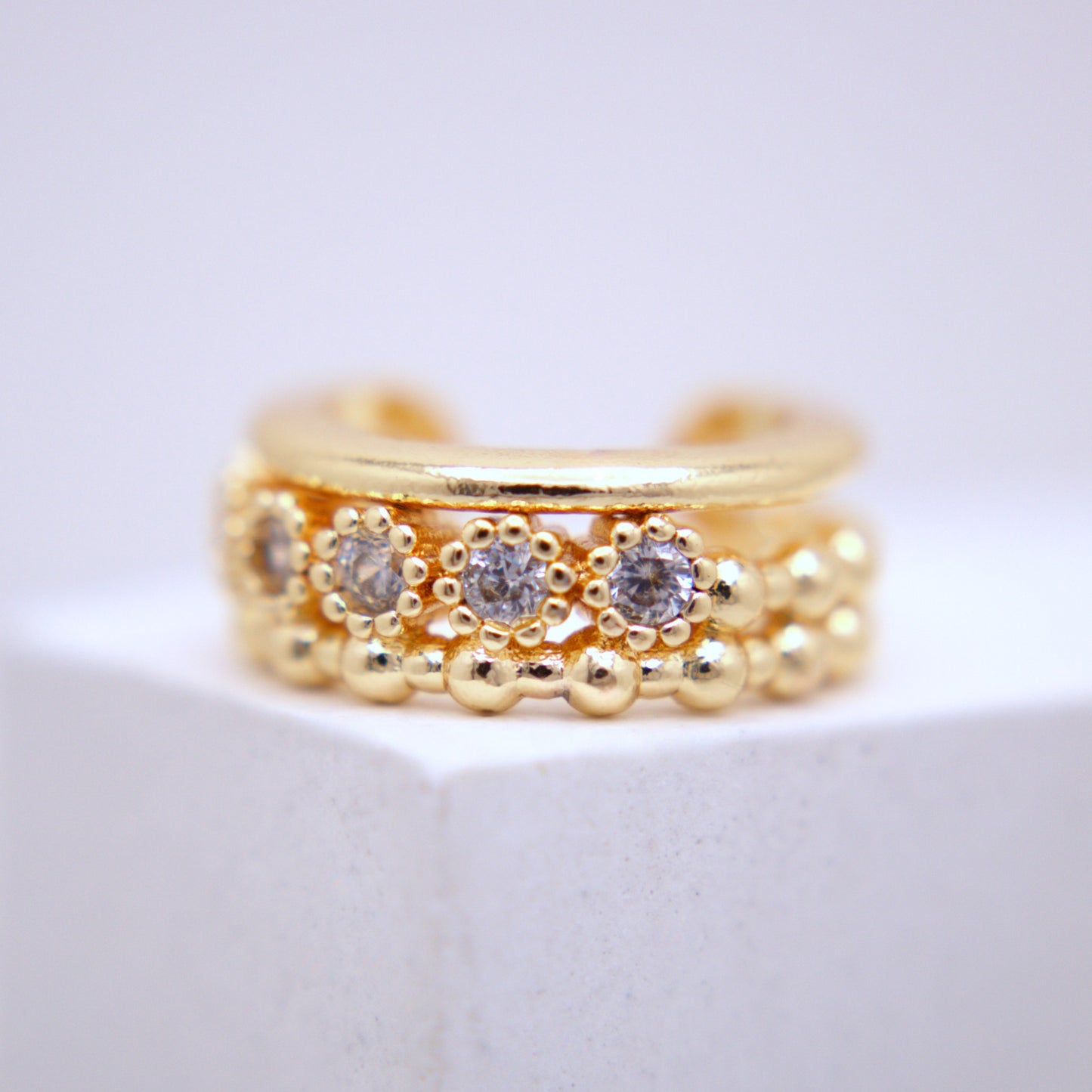 Gold ear cuff with embedded stones on a white background