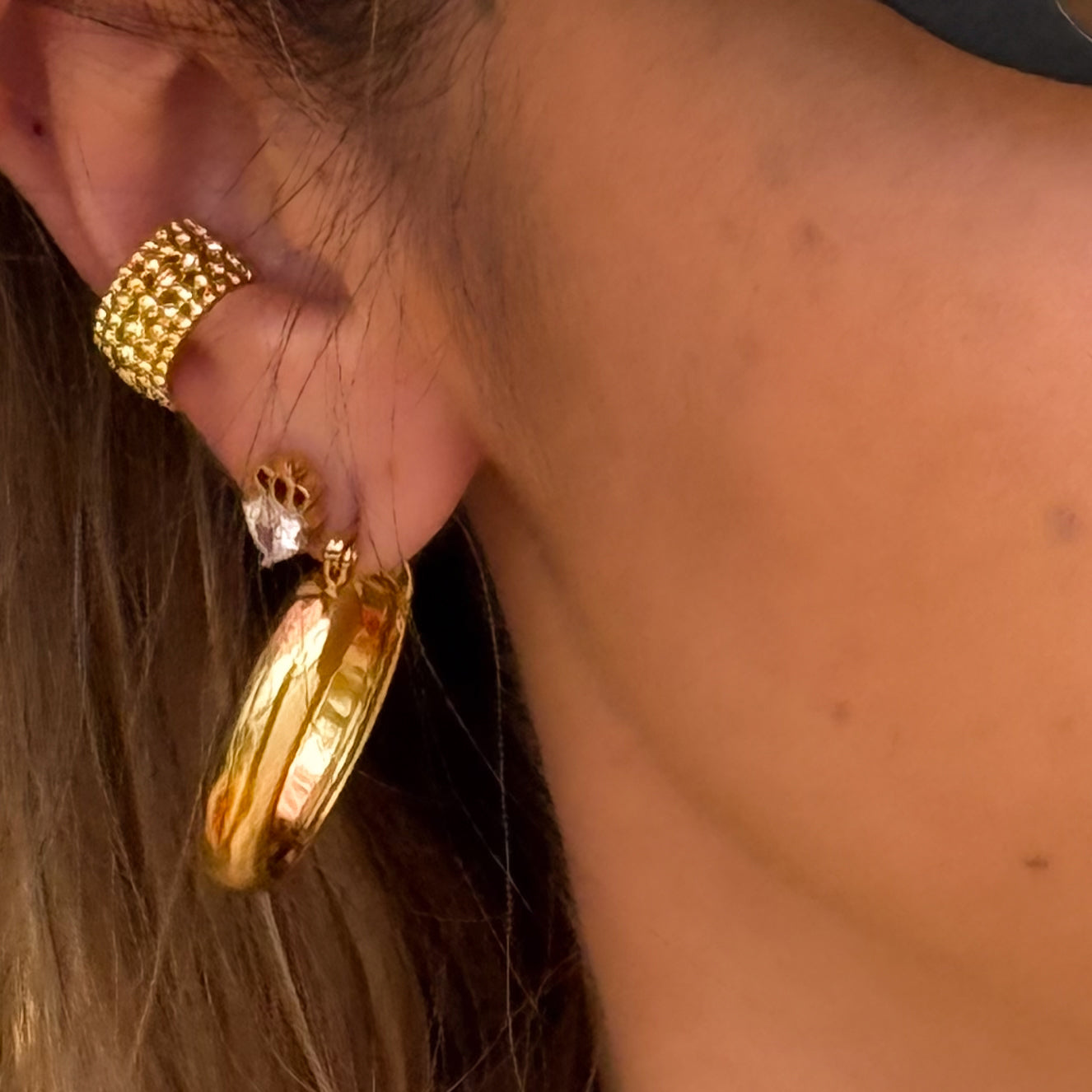 Close-up of a person wearing gold hoop earrings and a gold ring.
