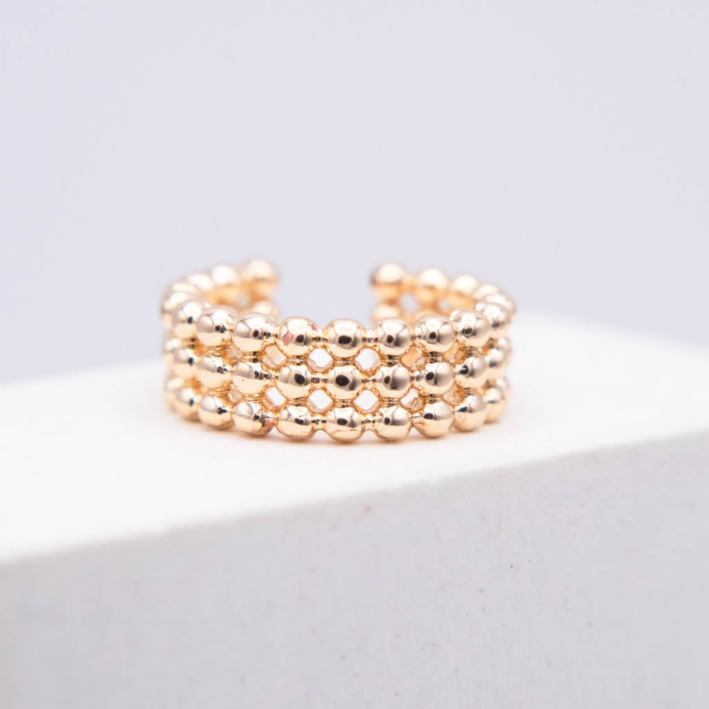 A rose gold beaded ring with three rows of small metallic beads, displayed on a white block against a light gray background.