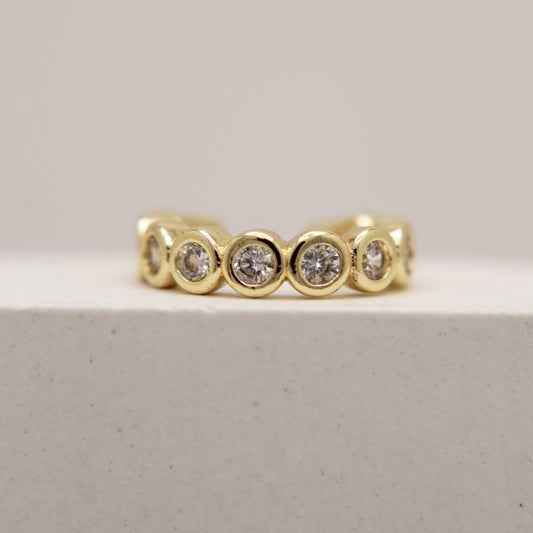 Gold ear cuff with embedded diamonds on a light gray background