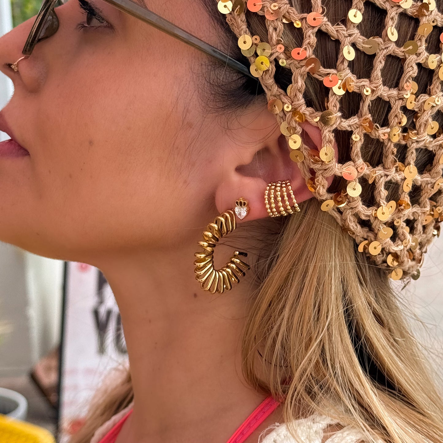 Close-up of a woman wearing gold hoop earrings and a sequined headpiece.