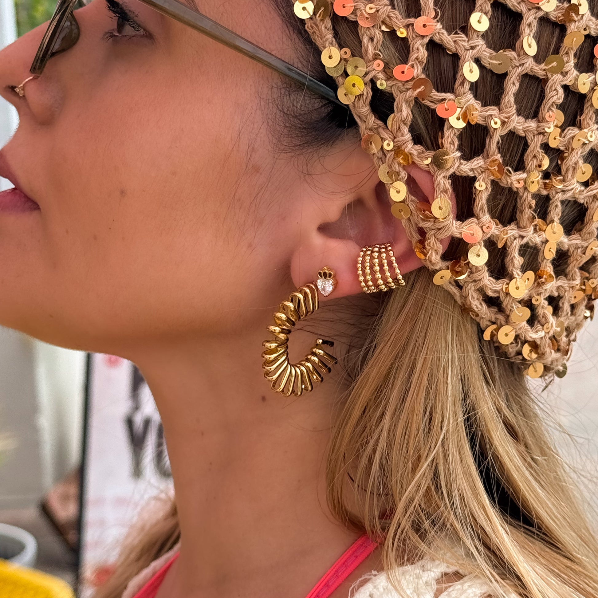 Close-up of a woman wearing gold hoop earrings and a sequined headpiece.