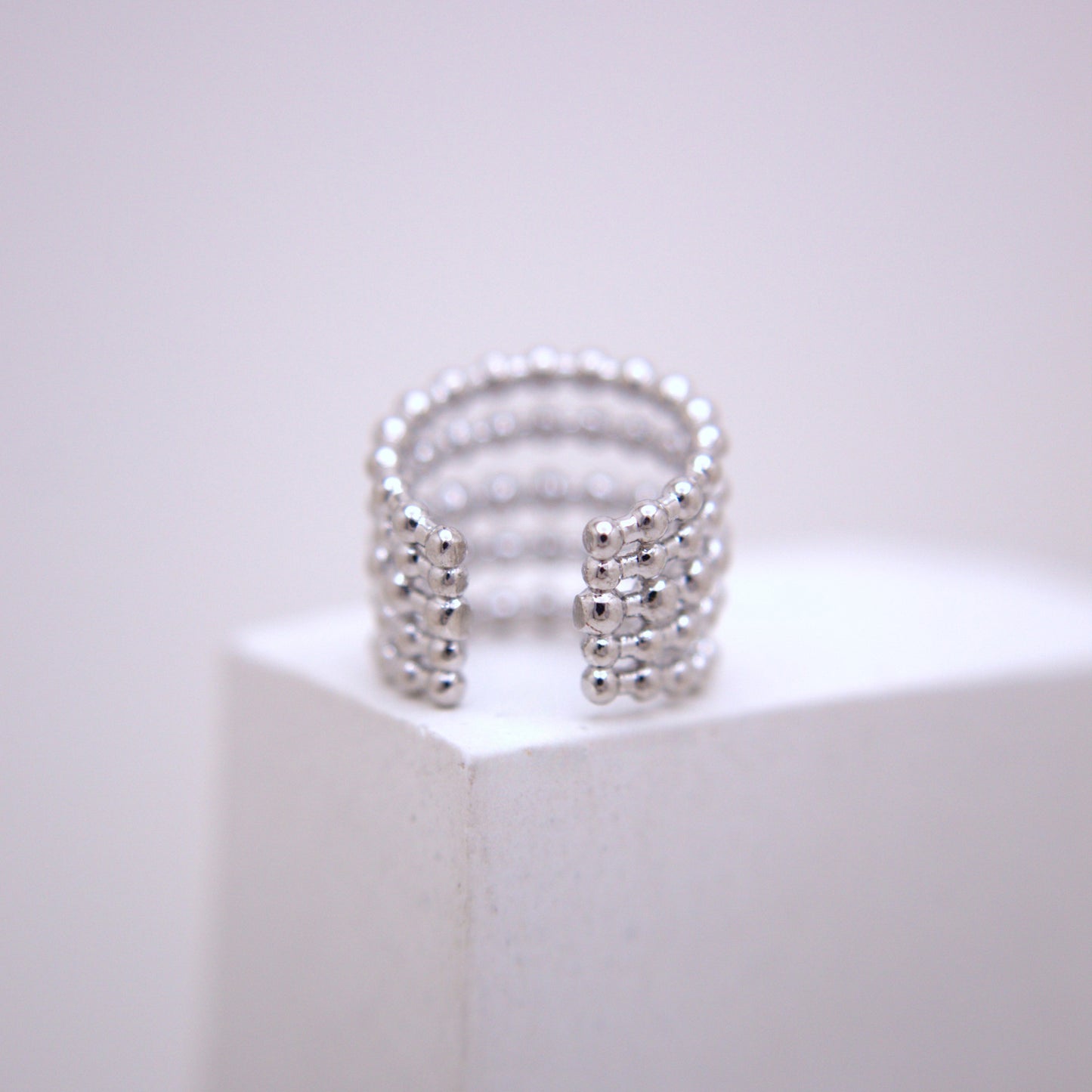Silver ear cuff on a white pedestal with a light gray background