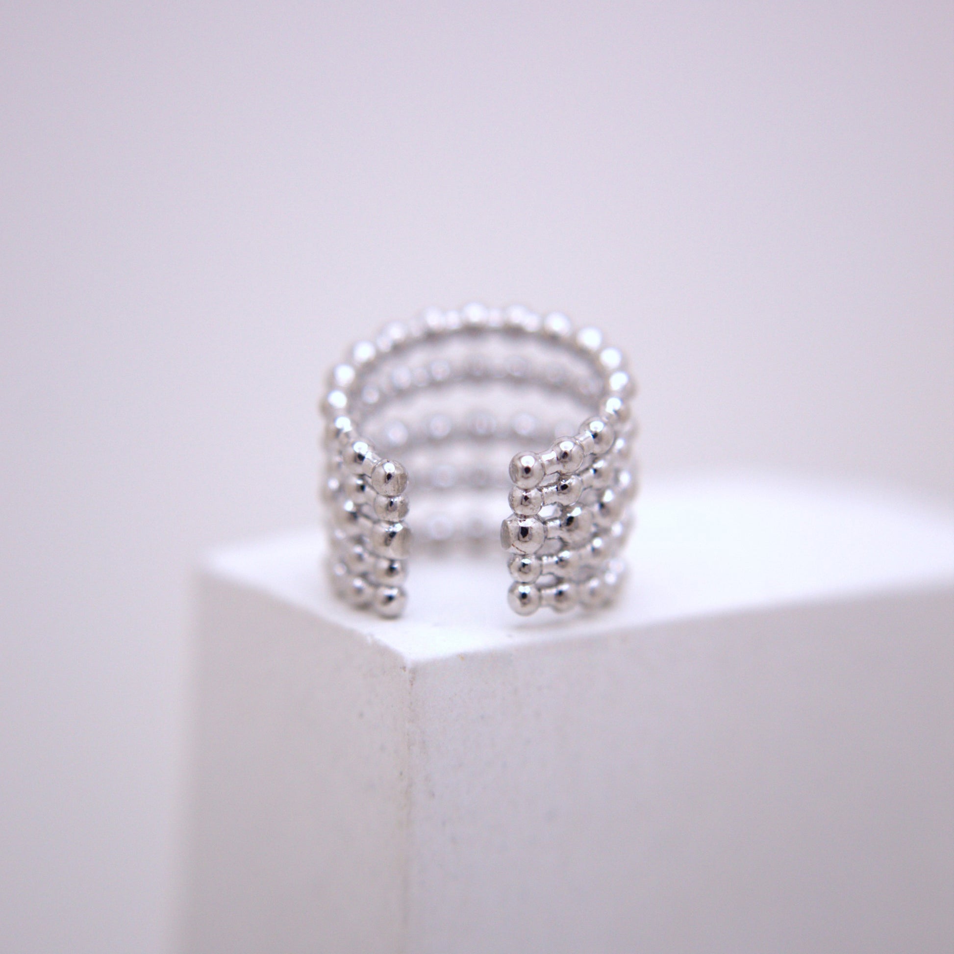 Silver ear cuff on a white pedestal with a light gray background