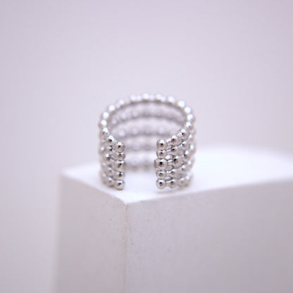 Silver ear cuff on a white pedestal with a light gray background