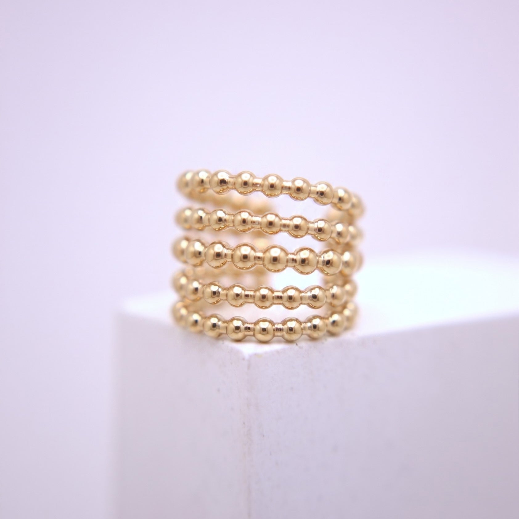 Gold beaded ear cuff on a white surface with a light purple background