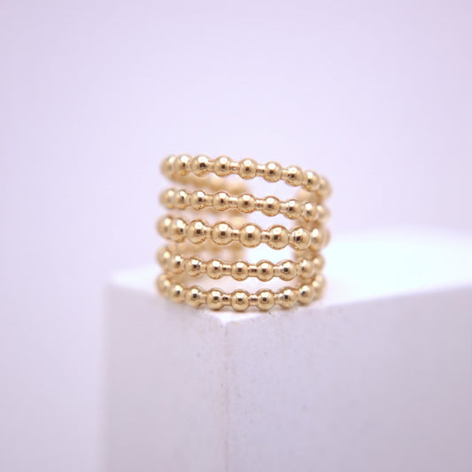 Gold beaded ear cuff on a white surface with a light purple background