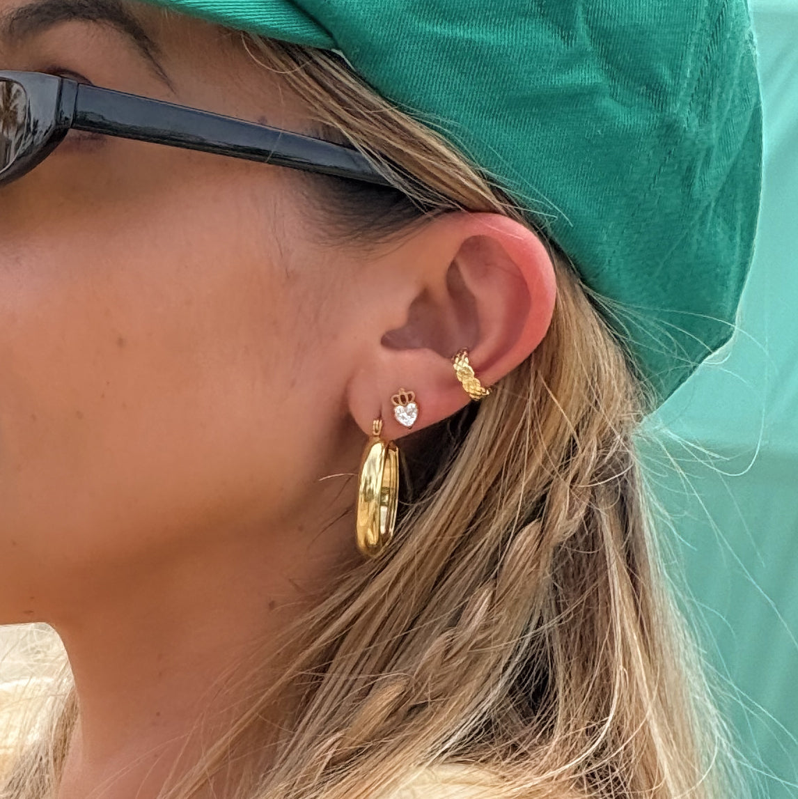 Close-up of a person wearing gold hoop earrings with a teal hat and sunglasses.