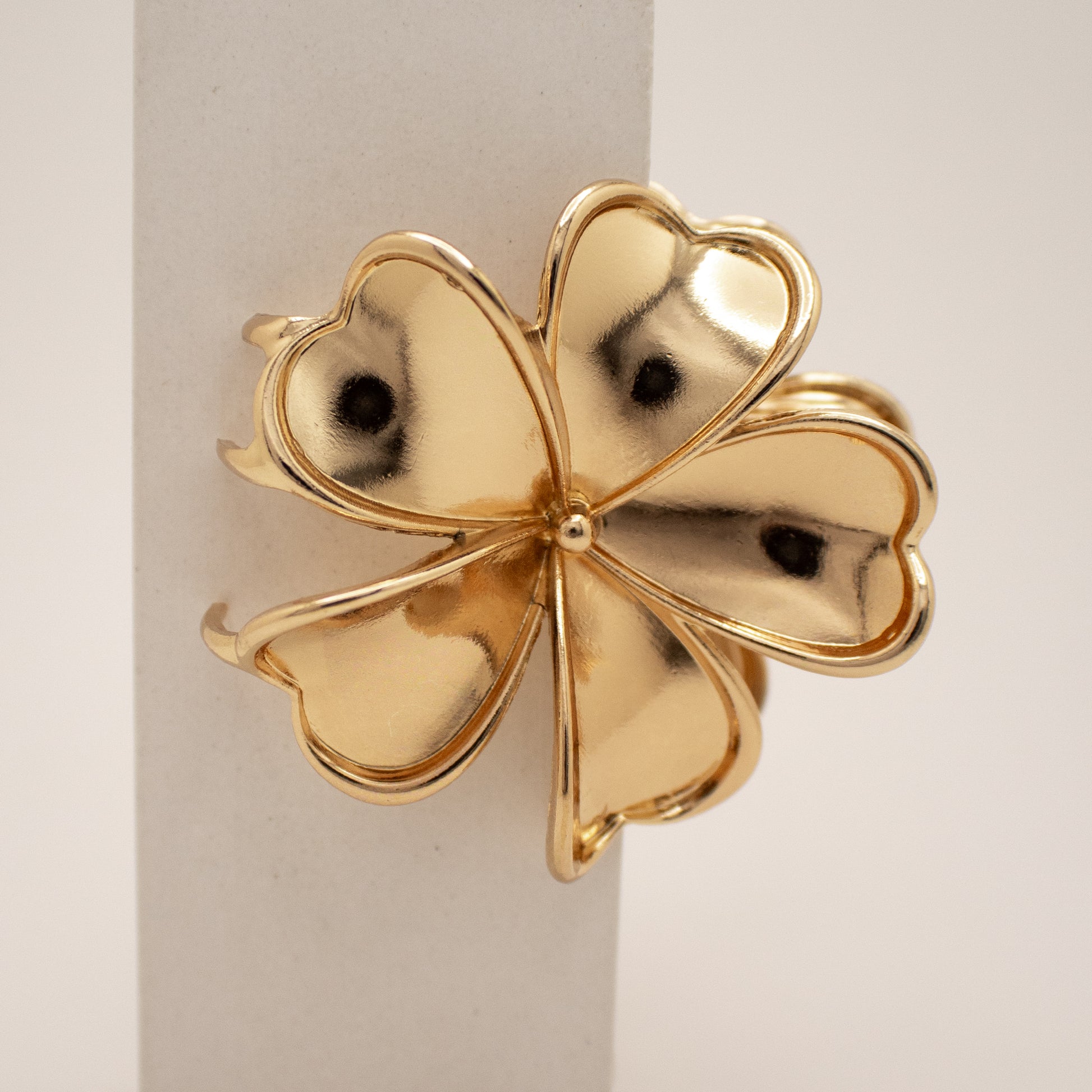 Gold four-leaf clover-shaped object on a light background