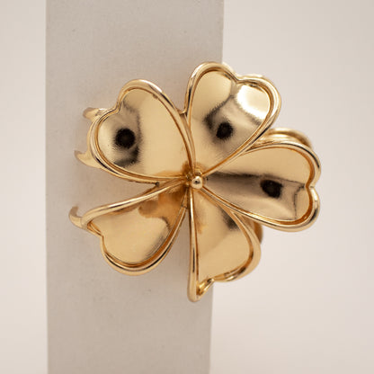 Gold four-leaf clover-shaped object on a light background
