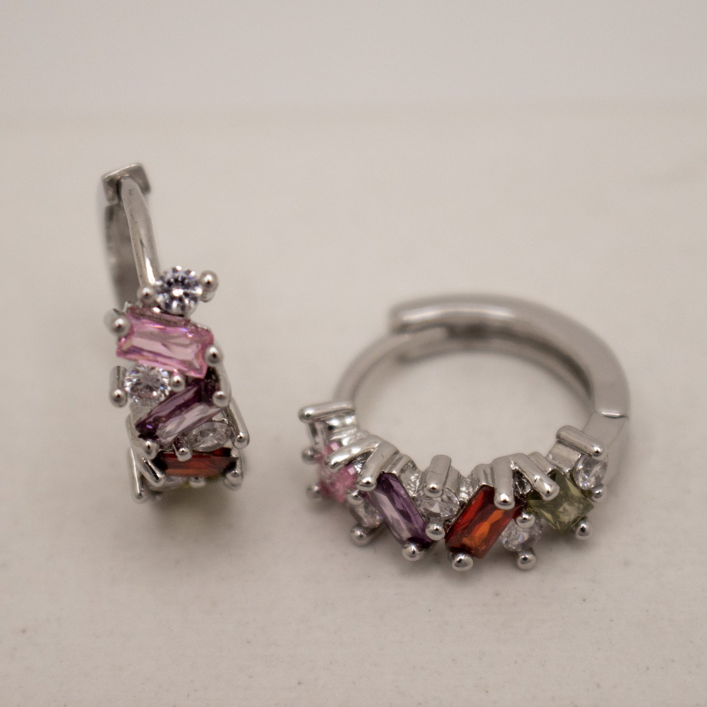 Pair of silver hoop earrings with multicolored gemstones on a light gray background