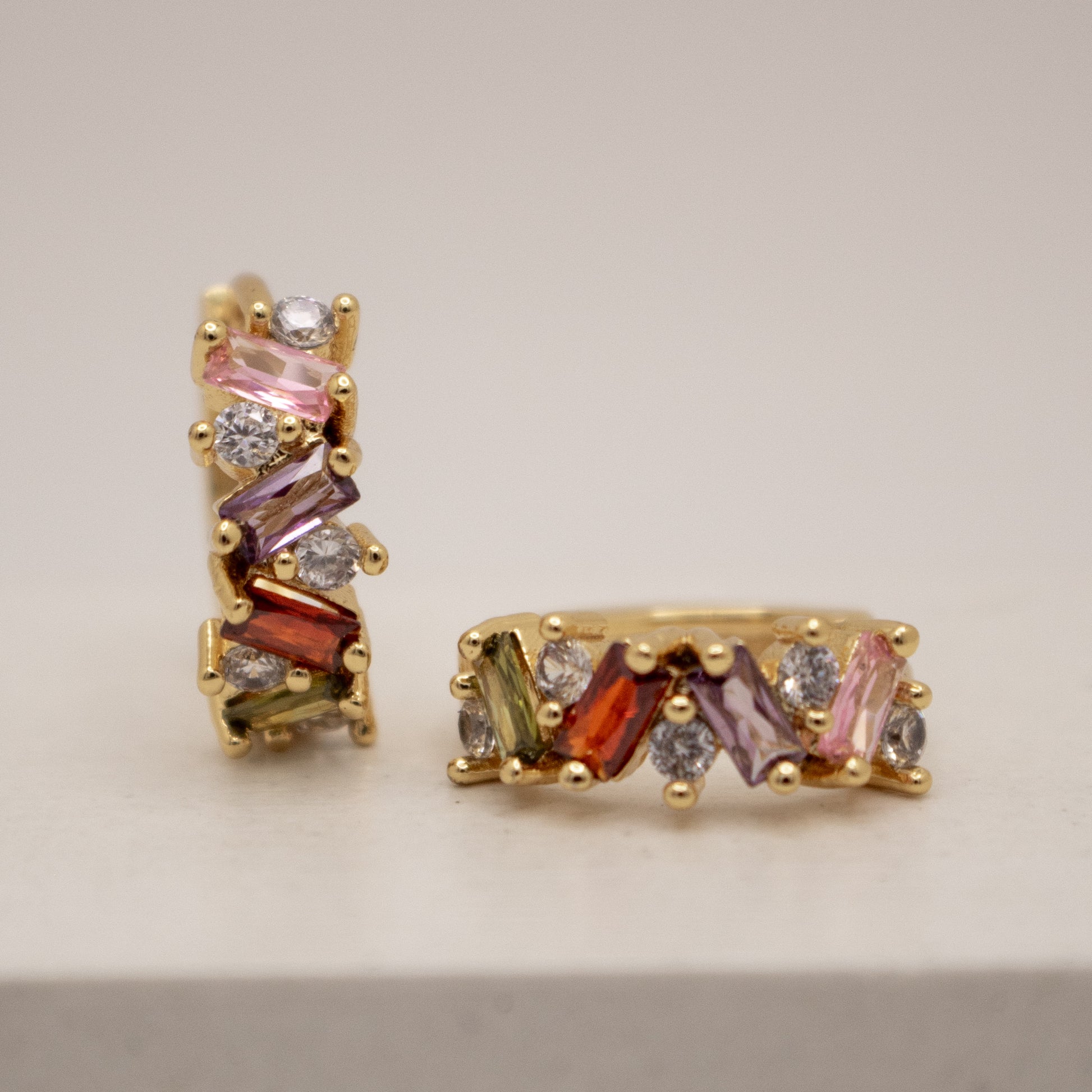 Gold earrings with multicolored gemstones on a beige background