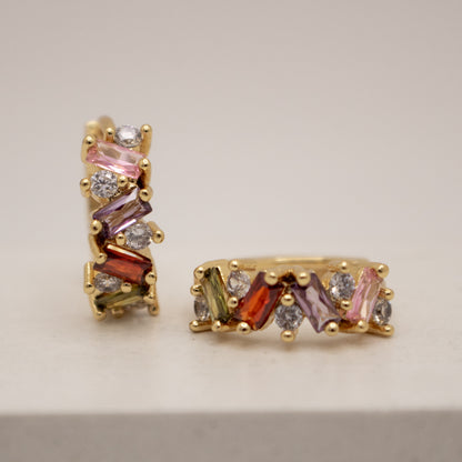 Gold earrings with multicolored gemstones on a beige background