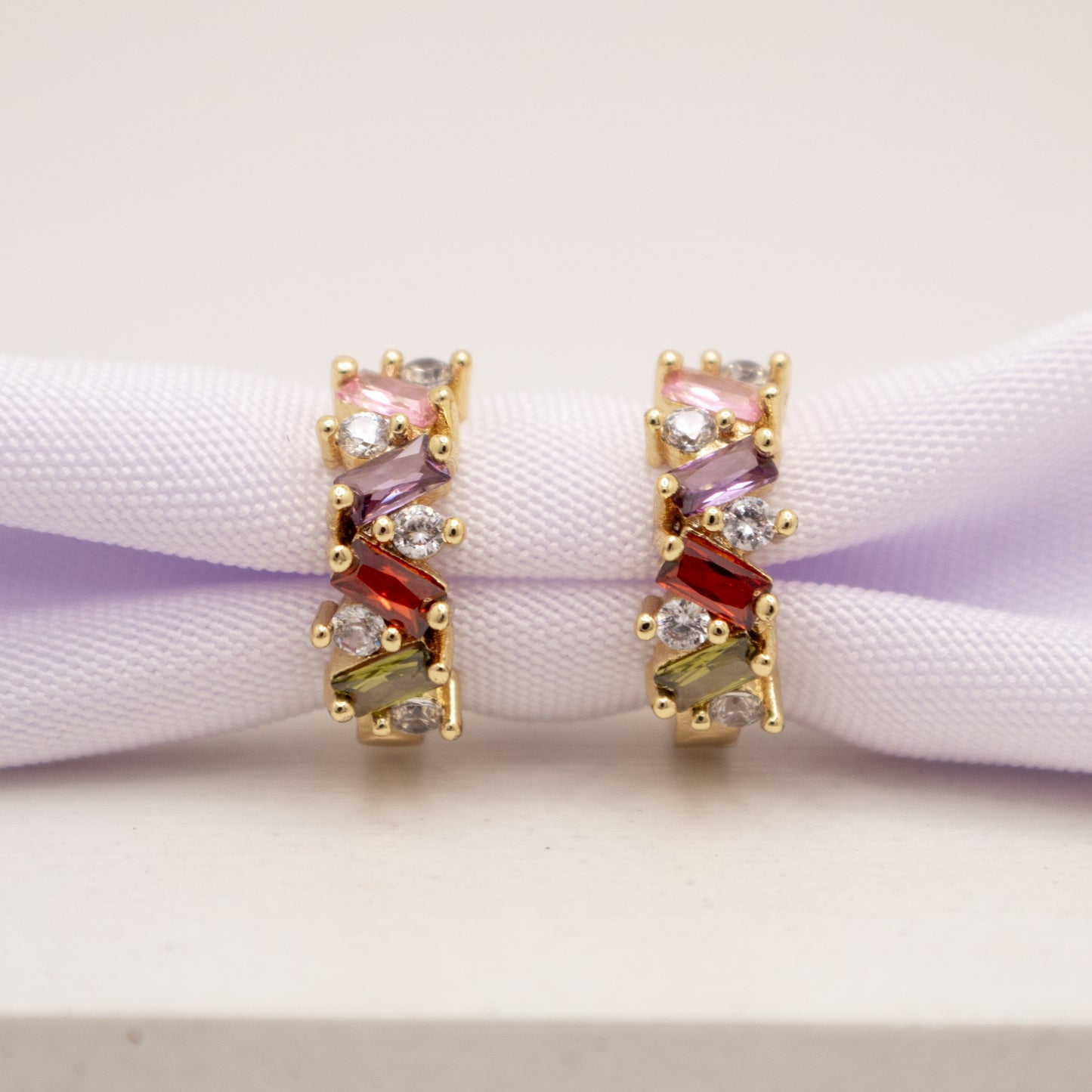 Pair of gold earrings with multicolored gemstones on a white surface