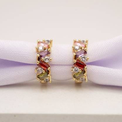Pair of gold earrings with multicolored gemstones on a white surface