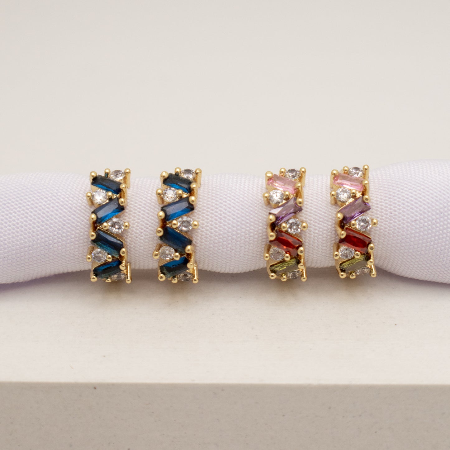 Pair of gold hoop earrings with colorful gemstones on a white background