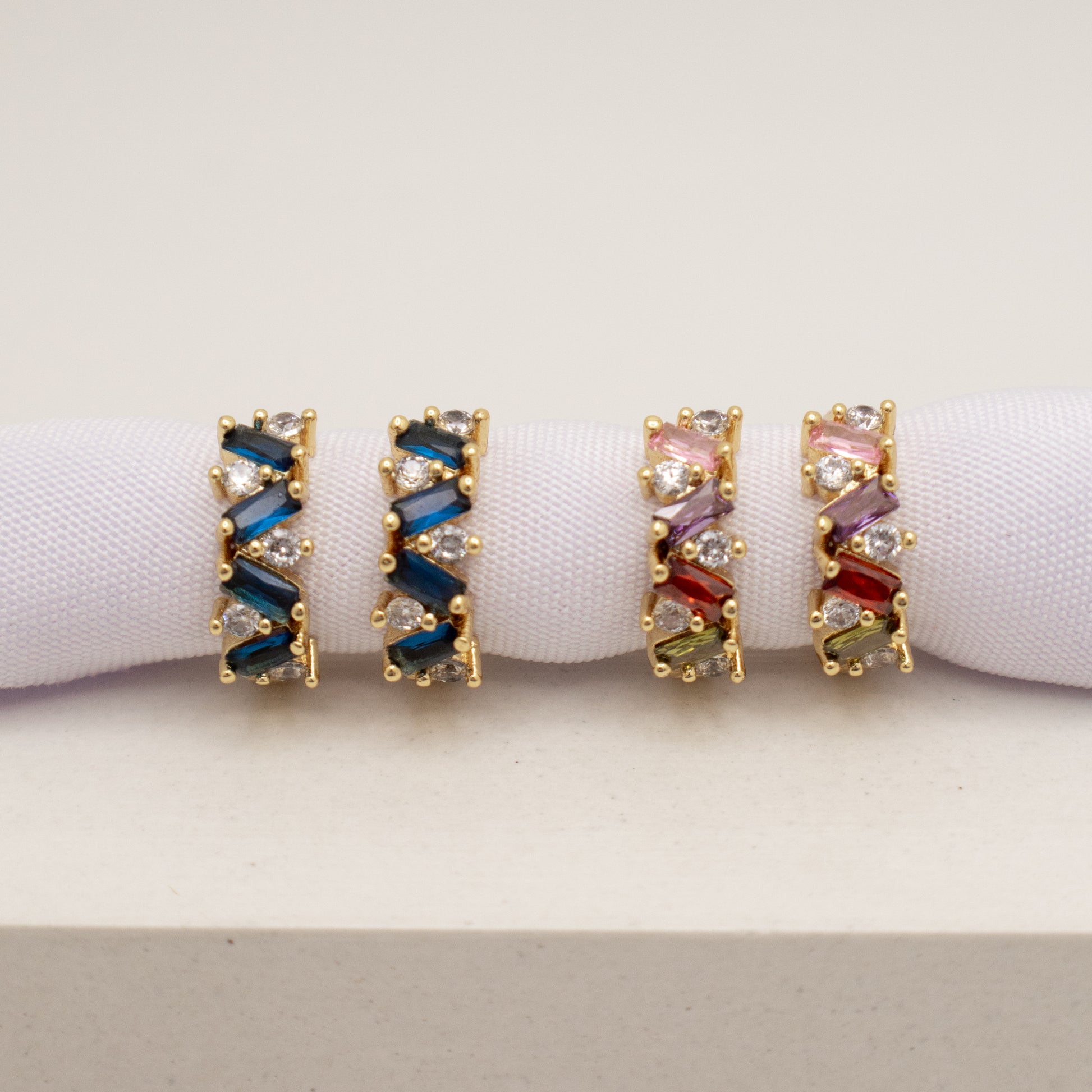 Pair of gold hoop earrings with colorful gemstones on a white background