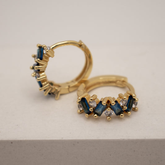 Gold hoop earrings with blue gemstones on a light gray background