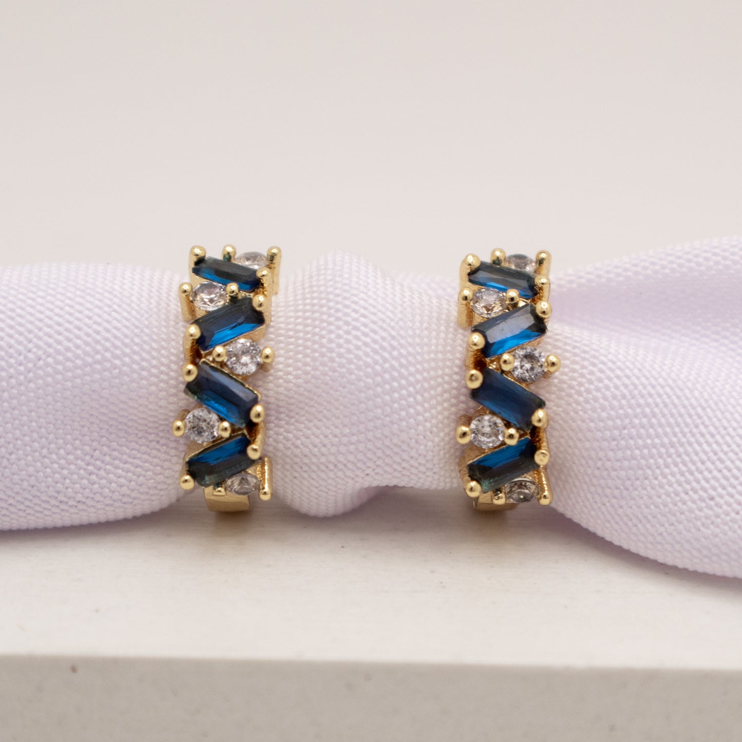 Gold earrings with blue and clear gemstones on a white background