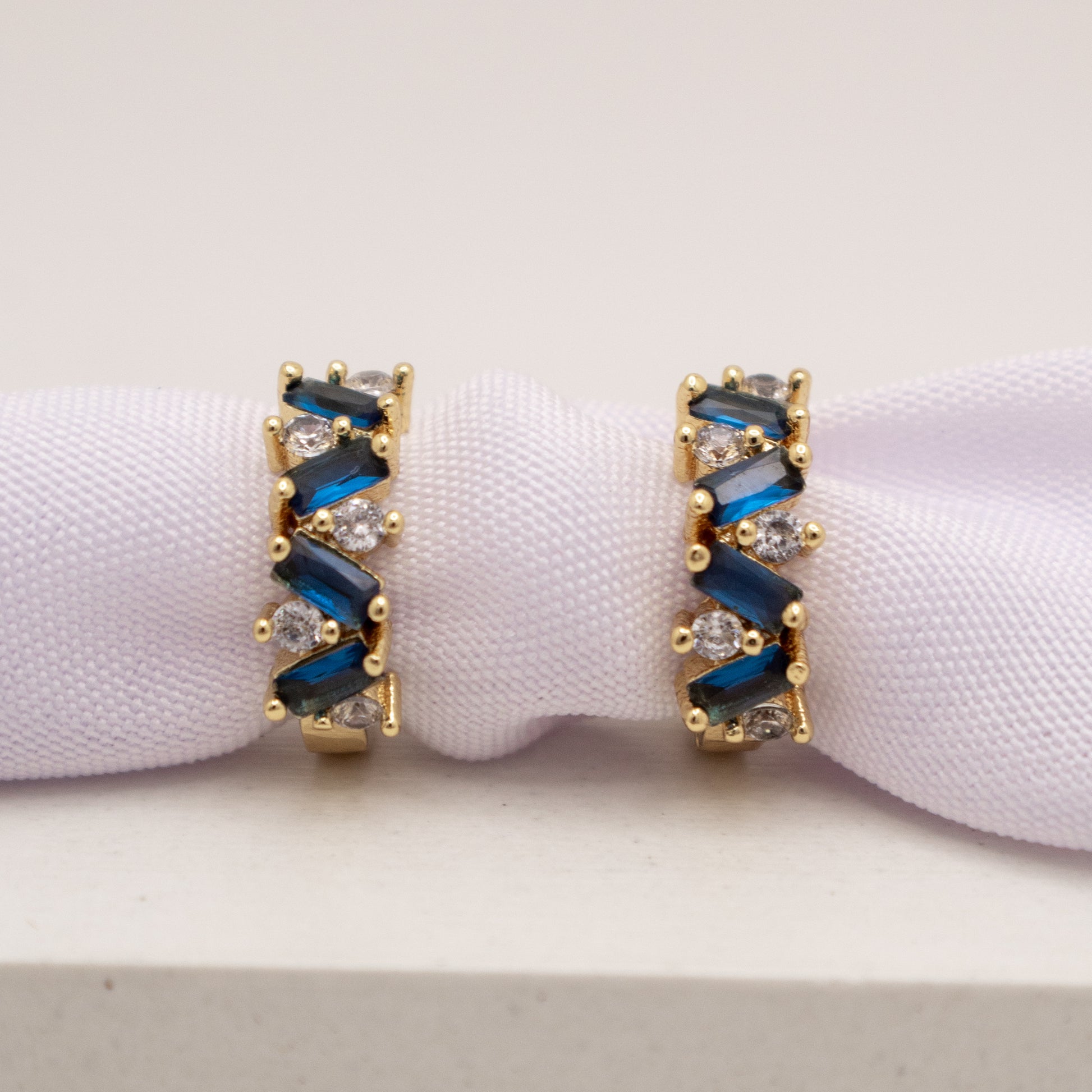 Gold earrings with blue and clear gemstones on a white background