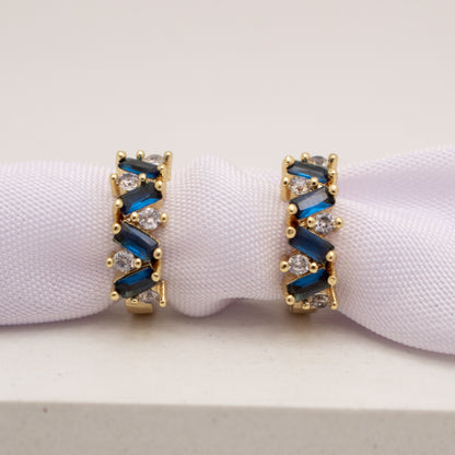 Gold earrings with blue and clear gemstones on a white background