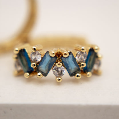Gold ring with blue gemstones and clear stones on a light background