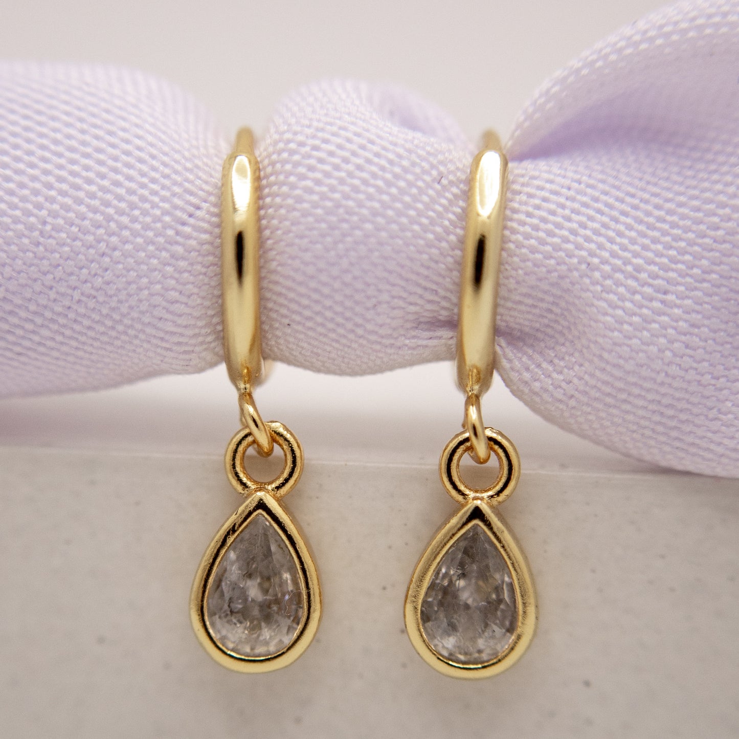Gold hoop earrings with teardrop-shaped gemstones on a white background