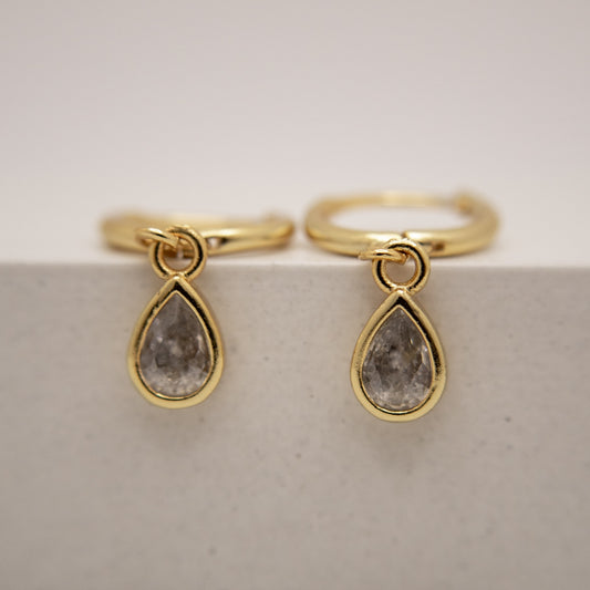 Gold earrings with teardrop-shaped gemstones on a light background
