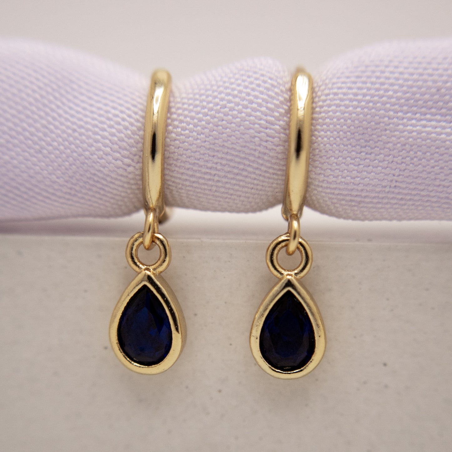 Gold earrings with teardrop-shaped blue gemstones on a white background