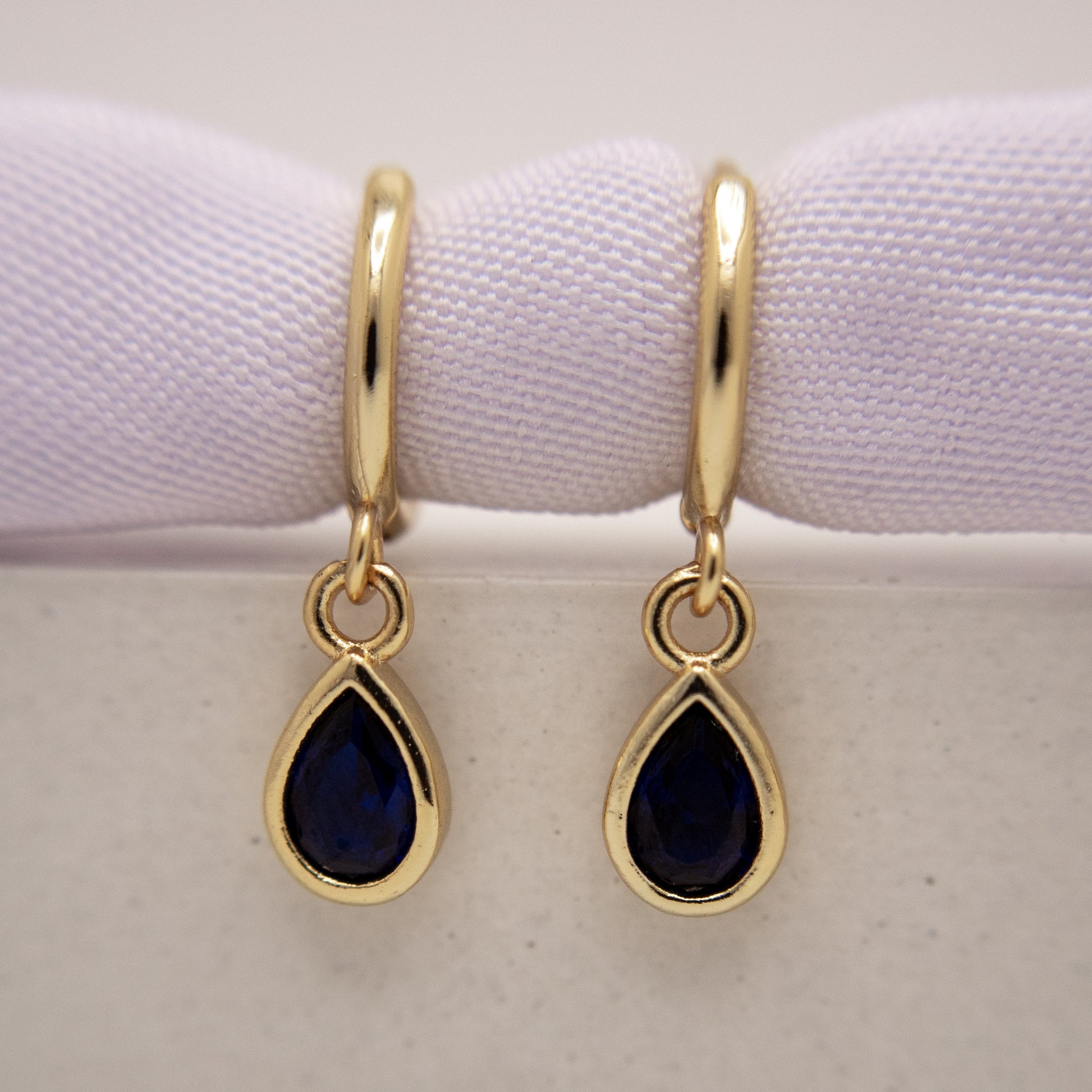 Gold earrings with teardrop-shaped blue gemstones on a white background