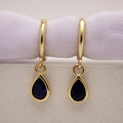 Gold earrings with teardrop-shaped blue gemstones on a white background