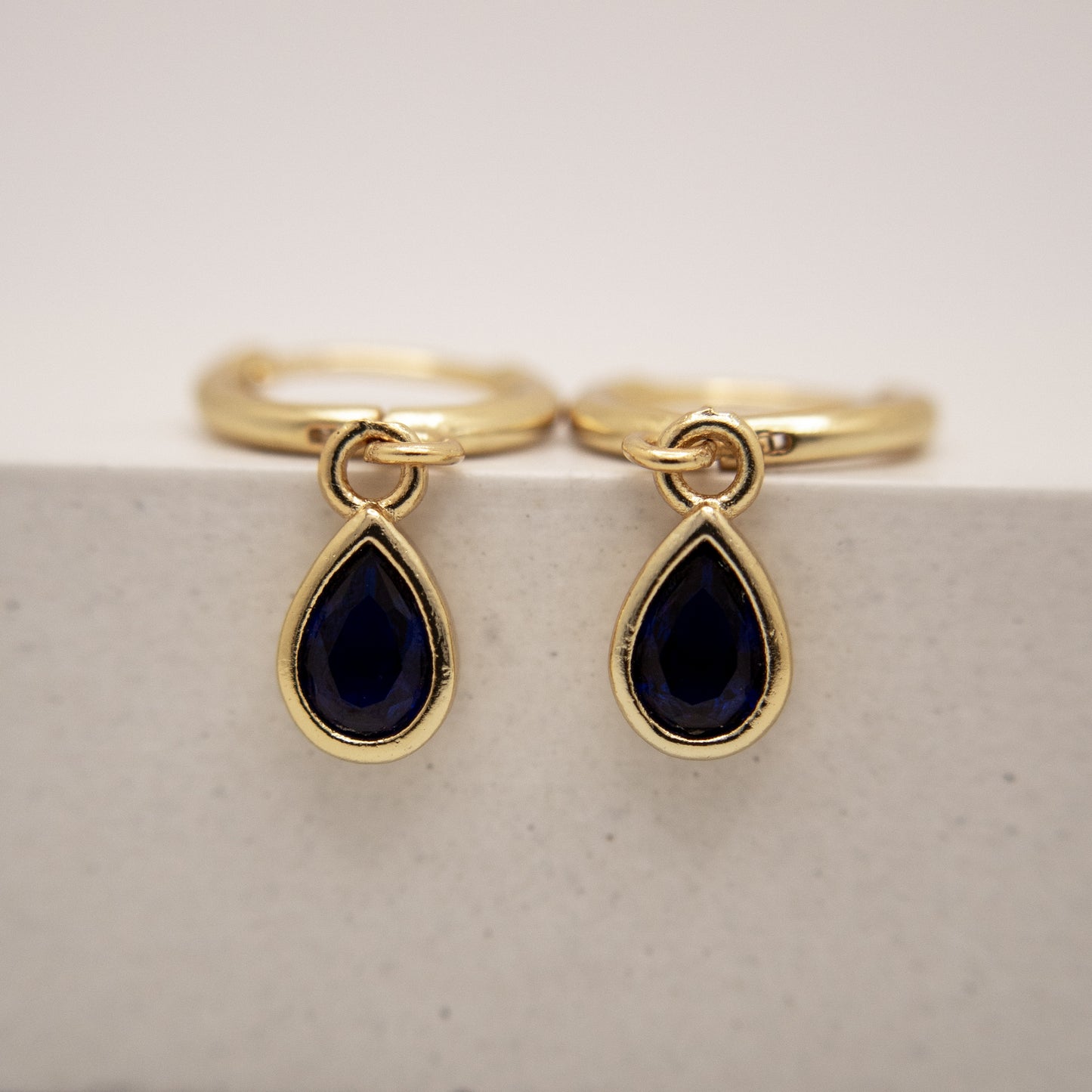Gold rings with teardrop-shaped black gemstones on a light gray background