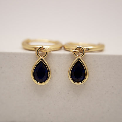 Gold rings with teardrop-shaped black gemstones on a light gray background