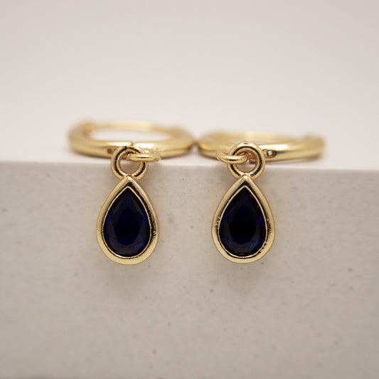 Gold rings with teardrop-shaped black gemstones on a light gray background