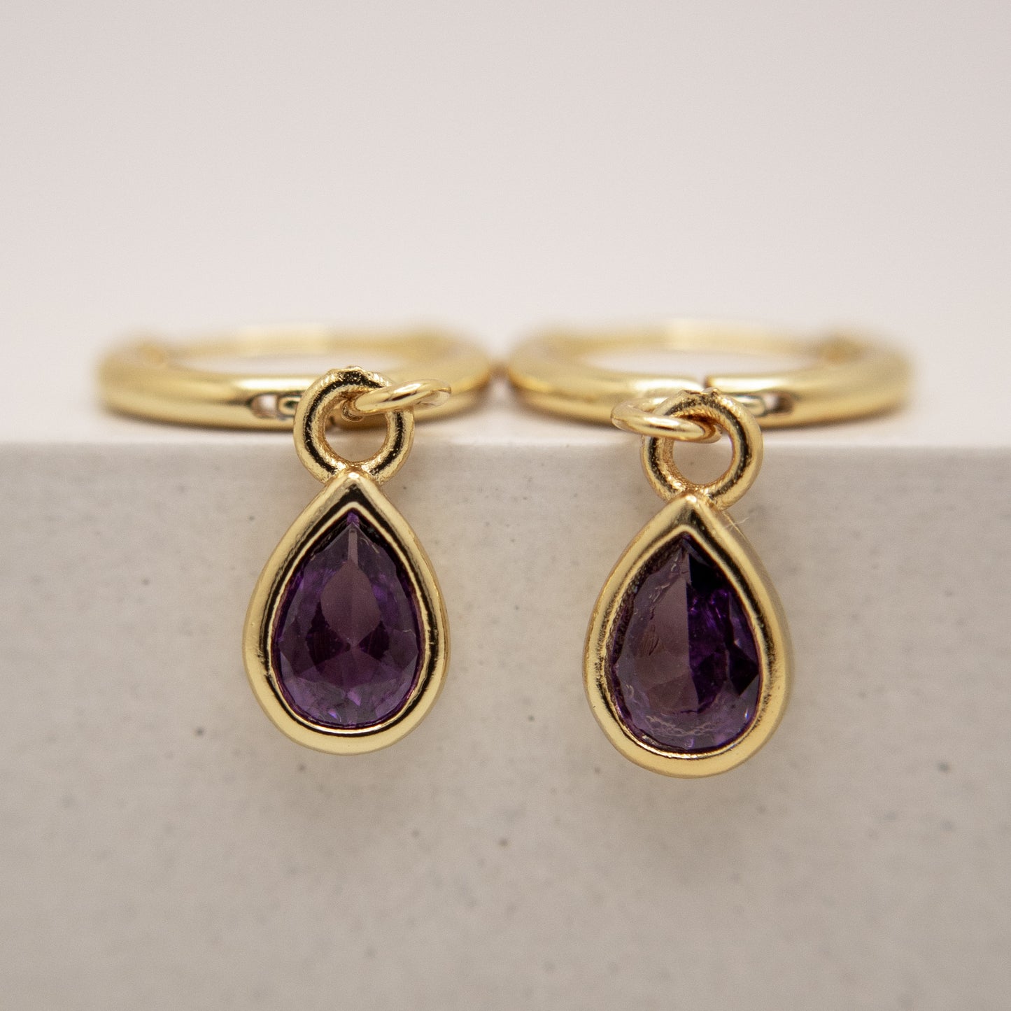 Gold rings with purple teardrop gemstones on a light background