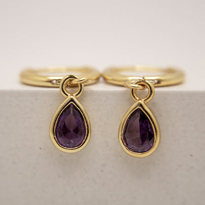 Gold rings with purple teardrop gemstones on a light background