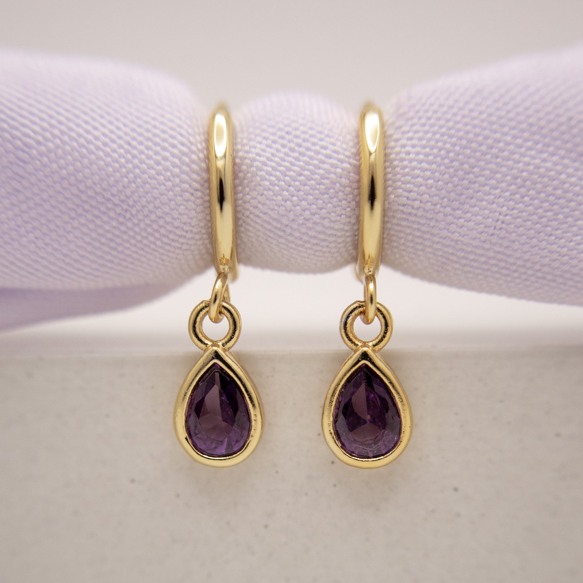 Gold earrings with purple gemstones on a white background