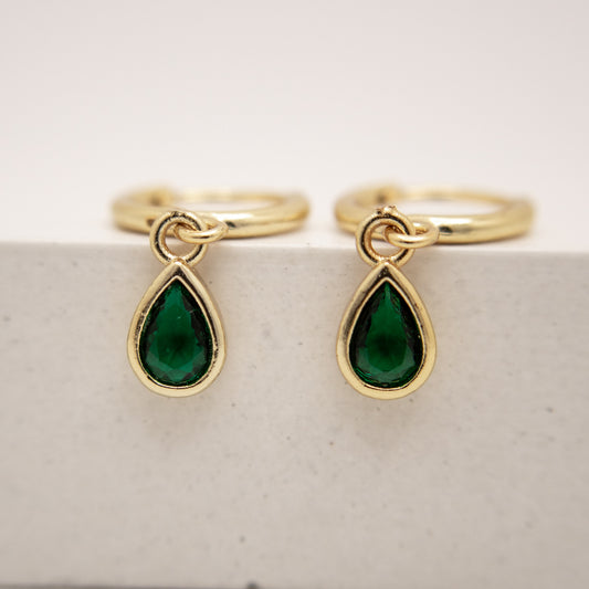 Gold rings with green teardrop charms on a light background