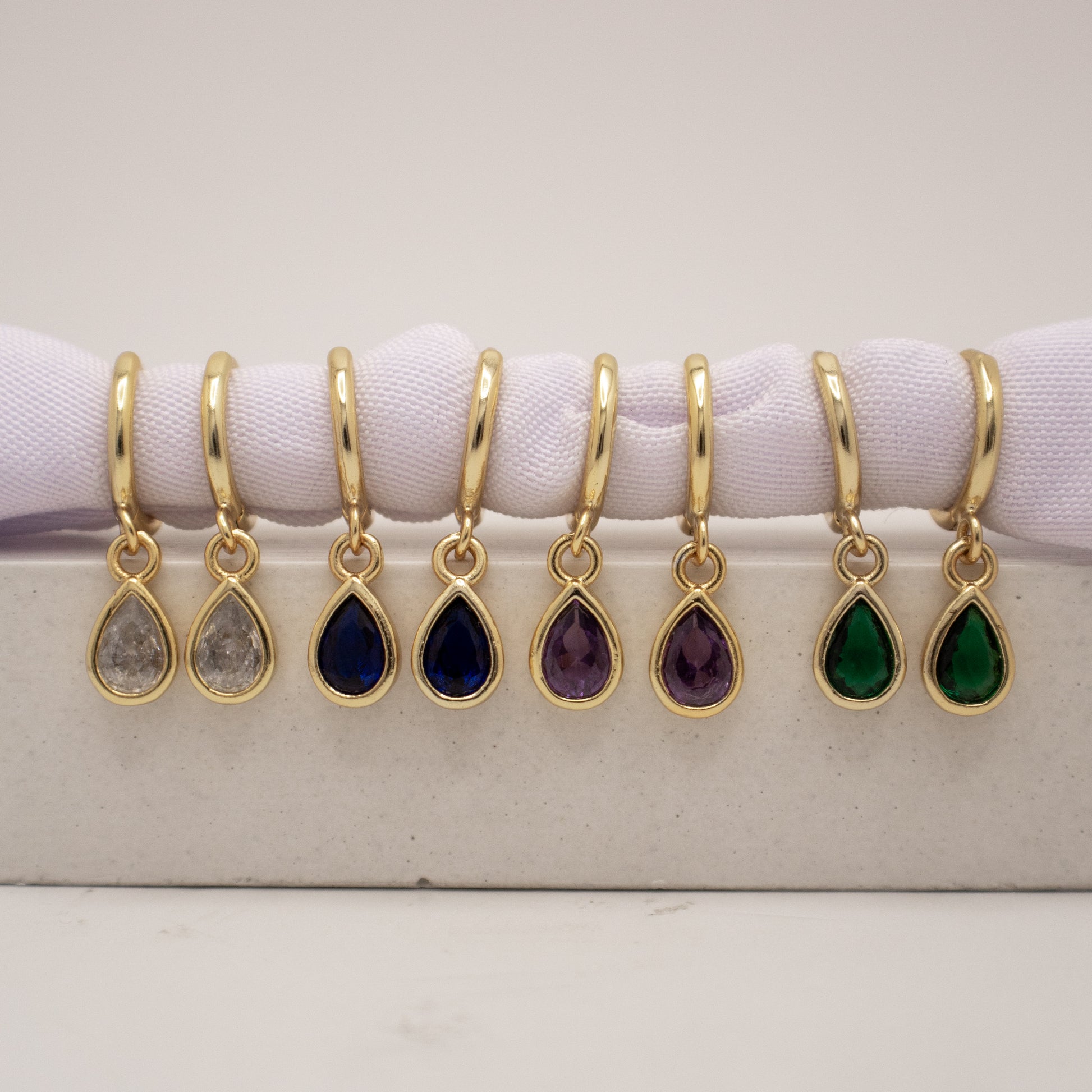 Gold teardrop earrings with colored stones on a white surface