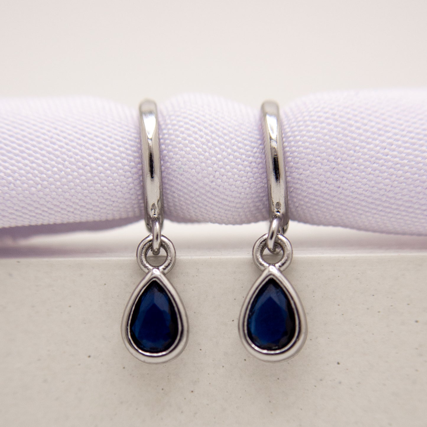 Teardrop-shaped blue gemstone earrings with silver hooks on a white background