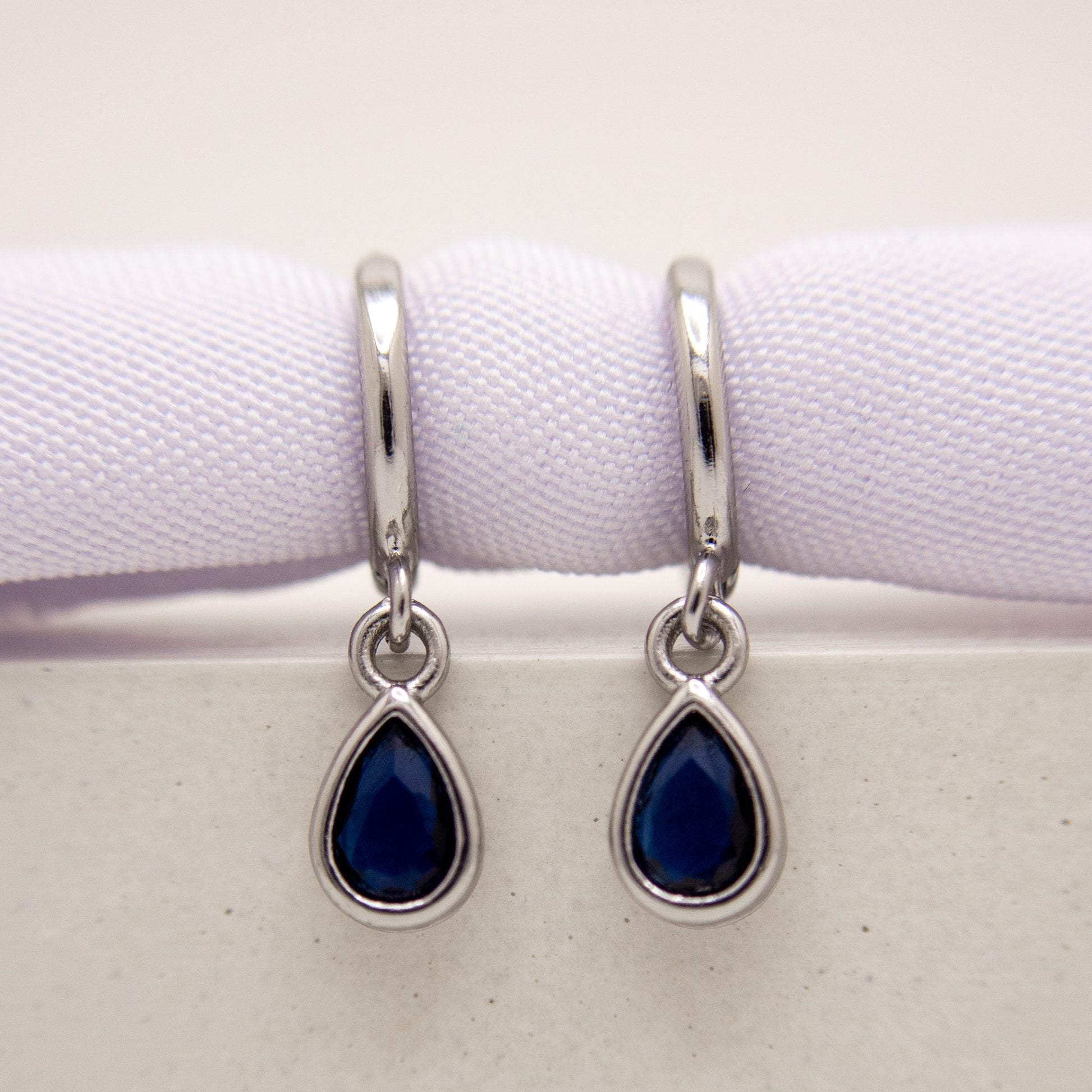 Teardrop-shaped blue gemstone earrings with silver hooks on a white background